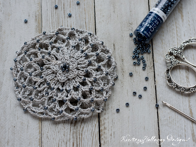 A beautifully beaded crochet bun cover hair accessory. It's made with grey crochet thread and blue beads.