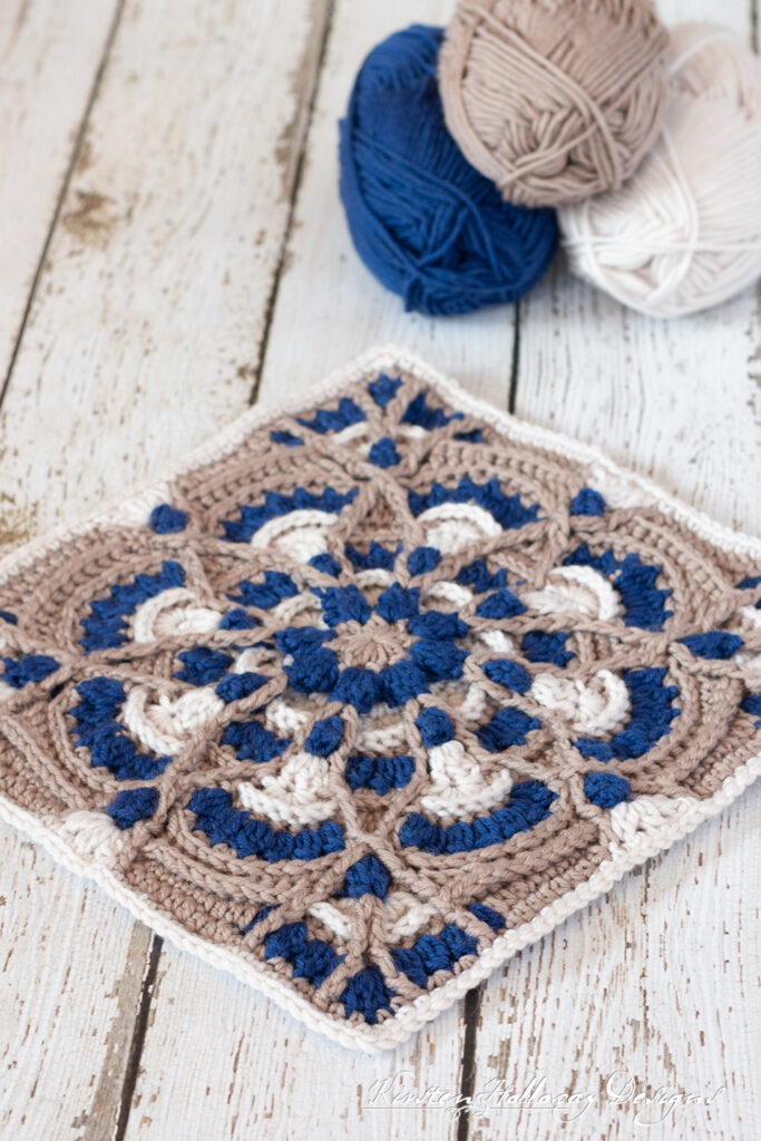 A textured crocheted afghan block made with tan, blue and white yarn.