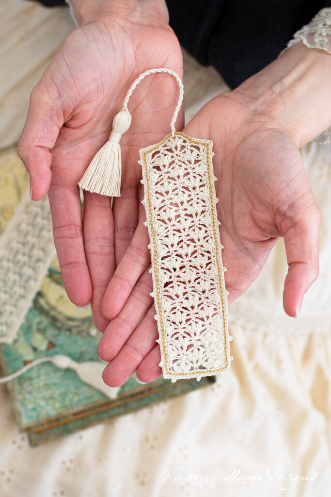 Closeup of a lacey crochet bookmark with gold trim in a woman's hands.