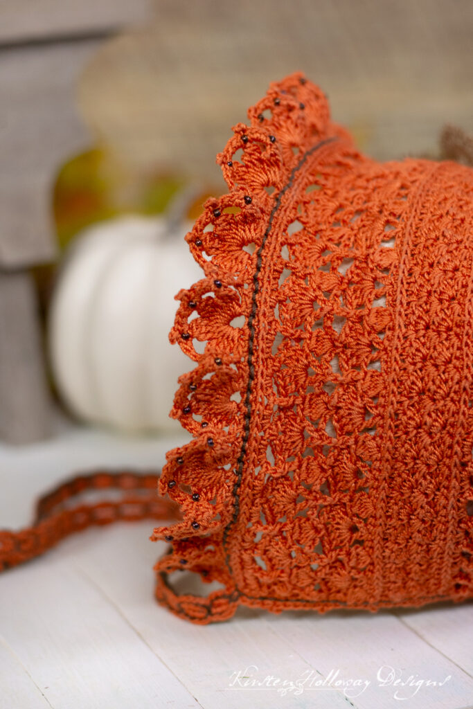 Close-up of lace with beadwork at front of orange crochet baby bonnet.