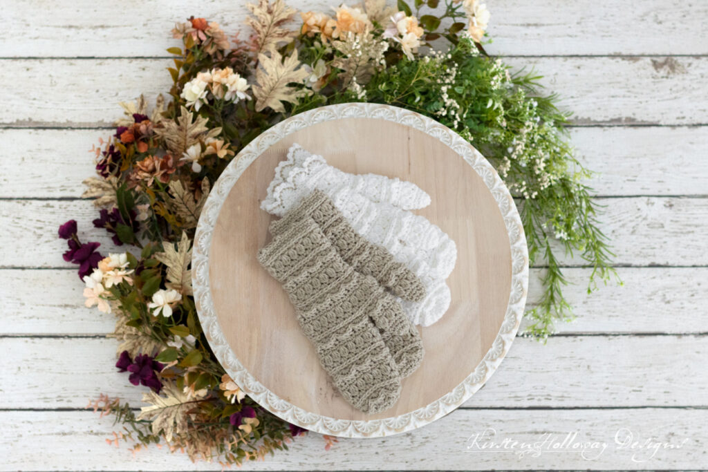 2 pairs of crochet mittens, taupe and white, on a round cake plate. Flowers ring the outside edge.